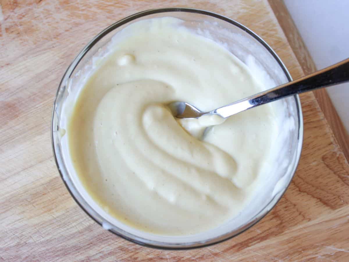 A small glass bowl with creamy white sauce and a spoon in it.