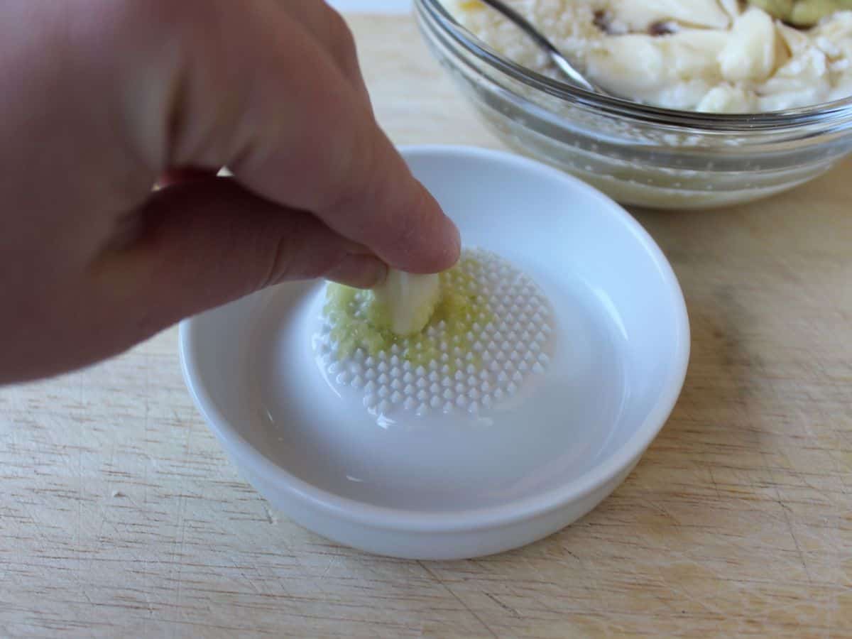 A garlic clove being grated using a round white ceramic grater.