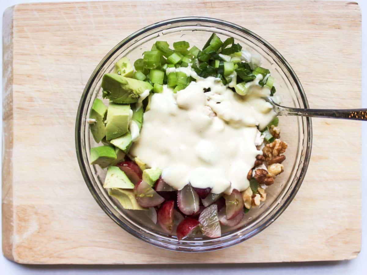 Chopped avocado, grapes, celery, walnuts with a spoonful of dressing on top in a glass bowl. The dressing is not mixed into the salad.