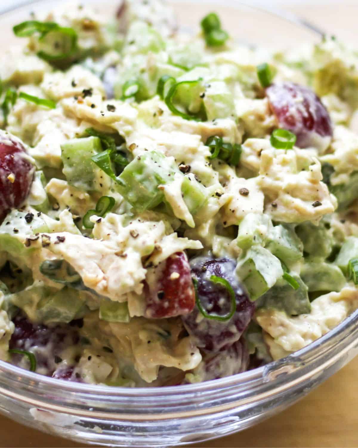 Close-up shot of California chicken salad with visible sliced red grapes, chicken meat, green veggies and a creamy dressing.