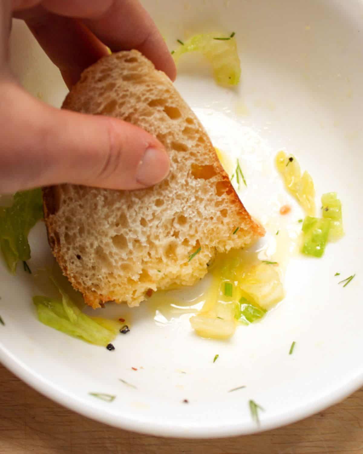 A white bowl with a few peaces of lettuce and oil. The bread is dipped into the oil.