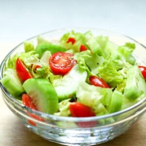 A glass bowl with a chopped salad consisting with chopped lettuce, sliced cucumbers and halved cherry tomatoes.