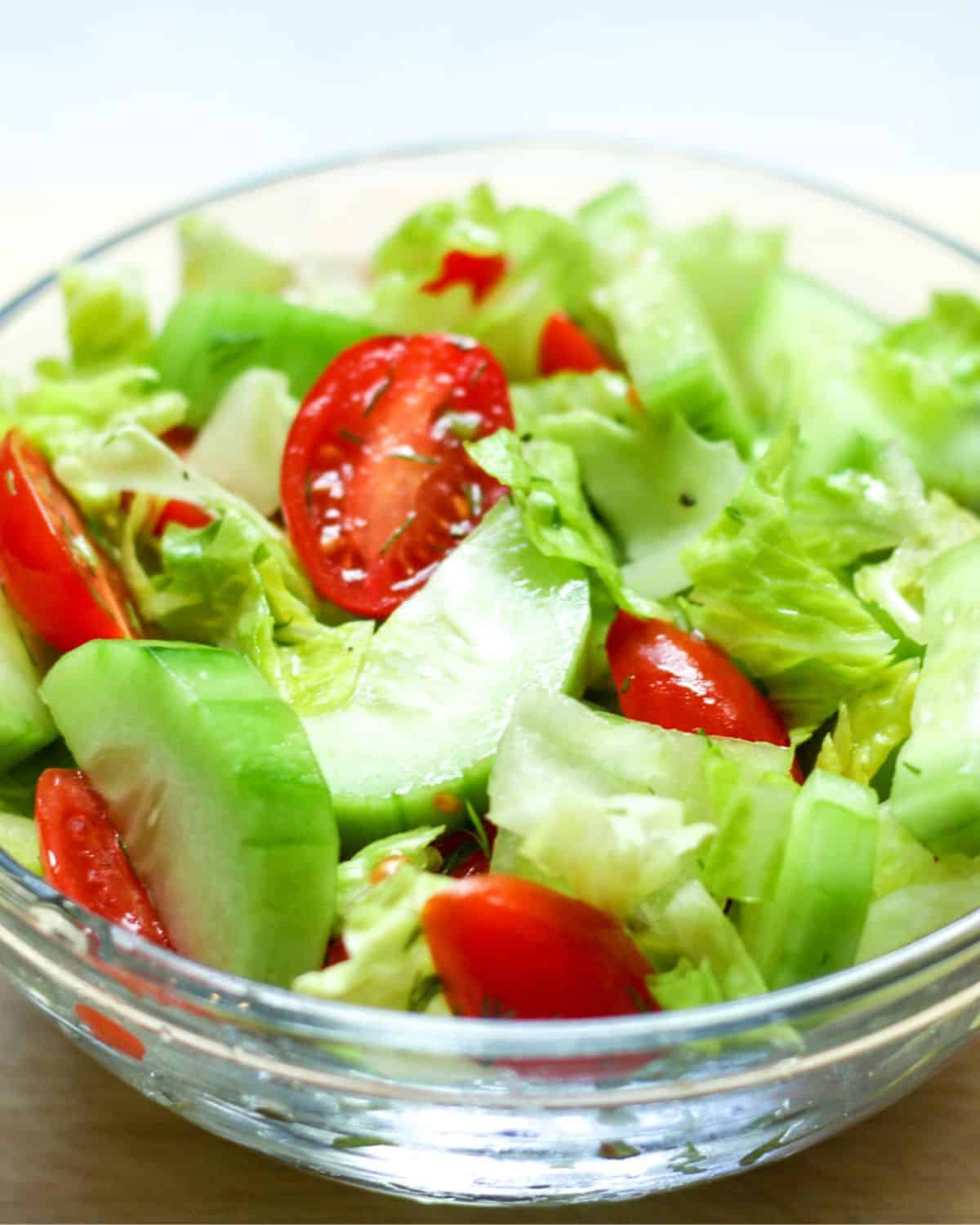 A glass bowl with a chopped salad consisting with chopped lettuce, sliced cucumbers and halved cherry tomatoes.