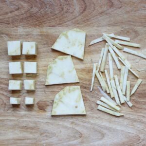 A cutting board with different cuts of celery root: cubed, sliced, julienne.