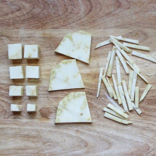 A cutting board with different cuts of celery root: cubed, sliced, julienne.