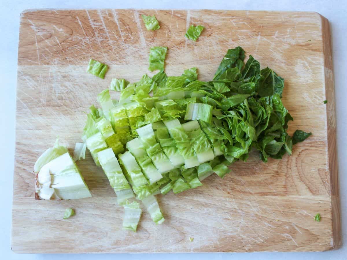 A head of green romaine lettuce chopped on a wooden cutting board.
