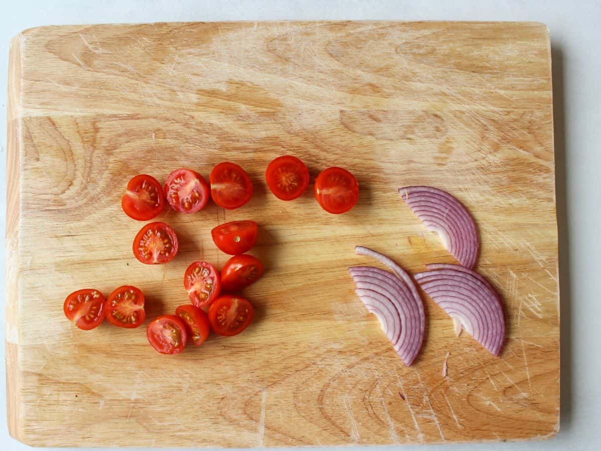 A cutting board with halved cherry tomatoes and sliced red onion.