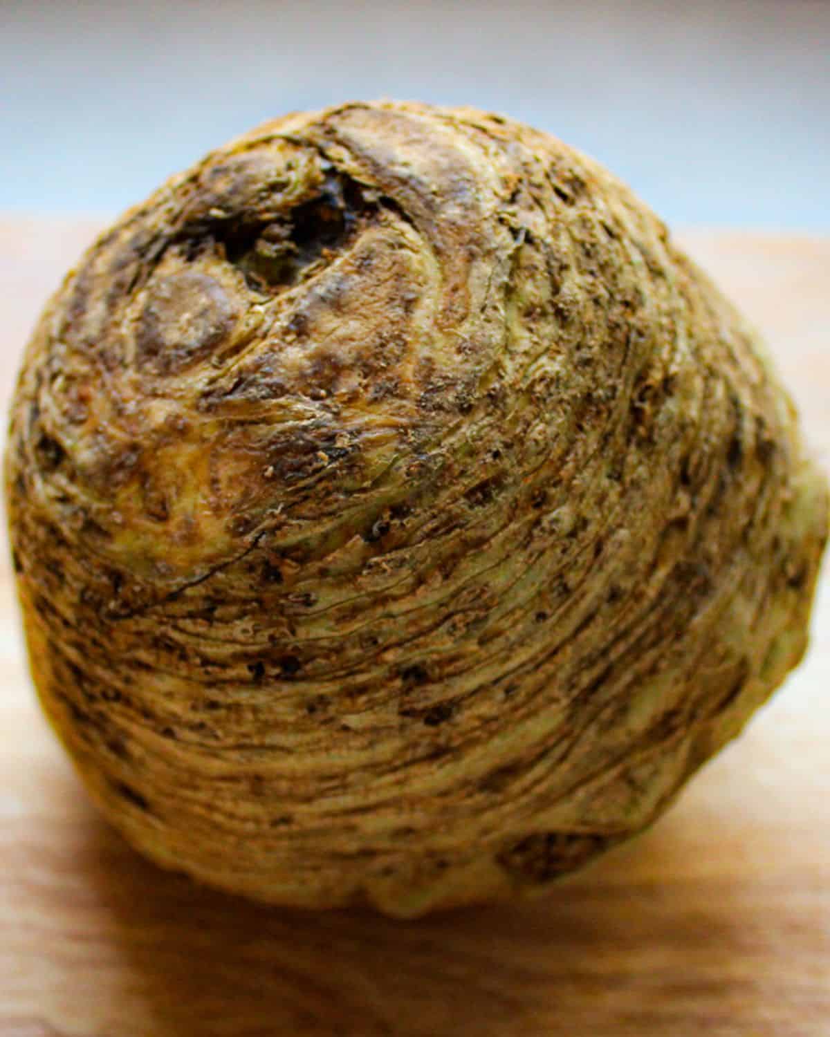 Brown, round root vegetable with bumpy, rough skin on a cutting boar.