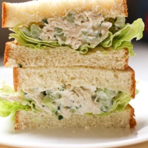 Two chicken sandwich halves stacked on top of each other. The sandwich is made with white bread, green lettuce and creamy chicken salad.