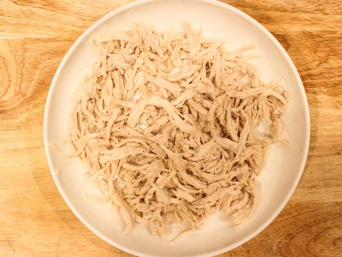 Shredded cooked chicken in a shallow white dish placed on a wooden surface.