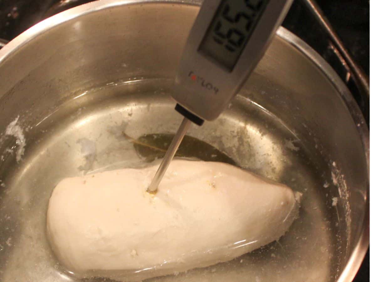 Poached whole chicken breast in a pot with water and the thermometer inserted into the meat showing 165°F.