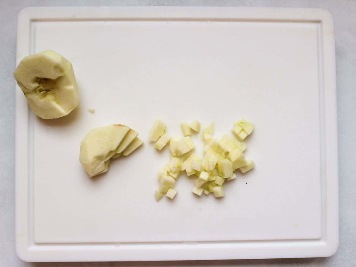 Heap of cubed apple, sliced apple and half of the peeled apple on white cutting board.