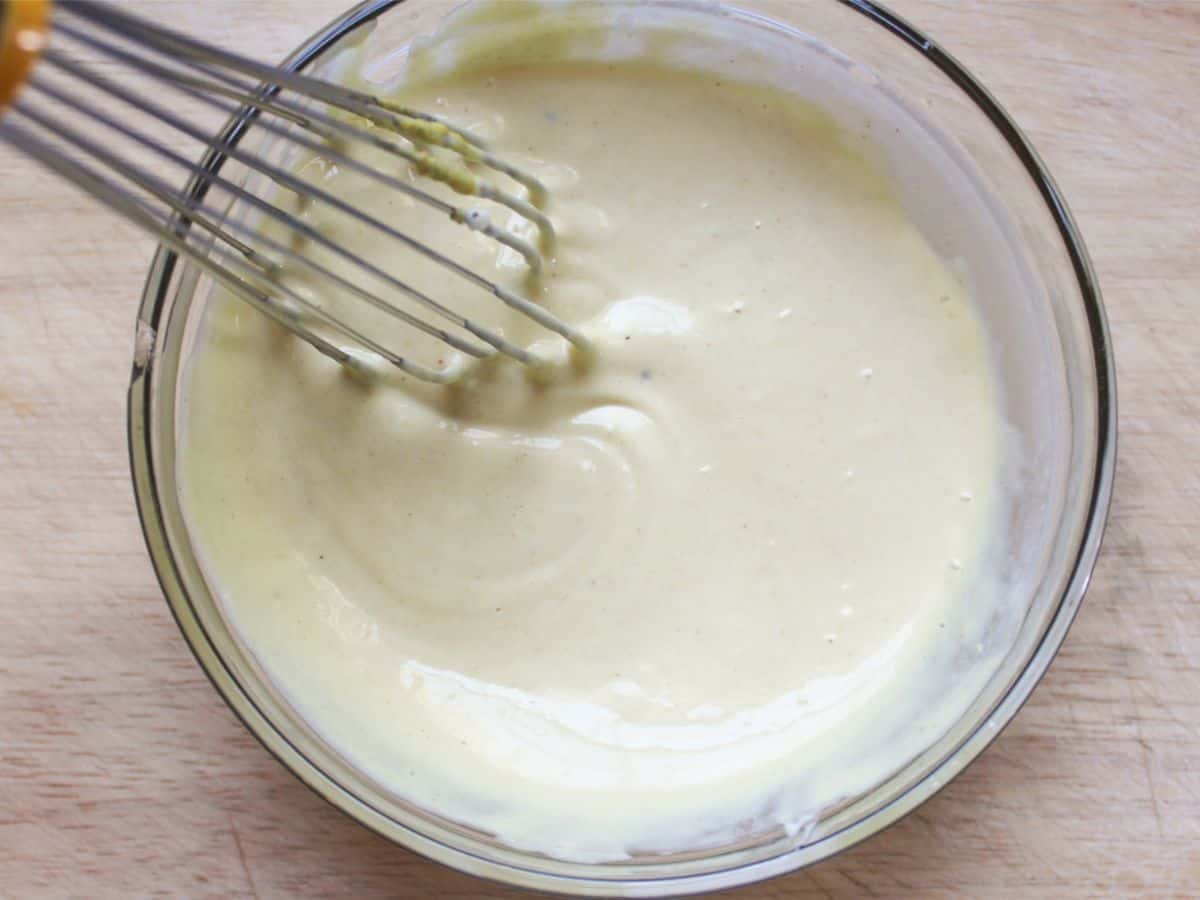 Ivory mayo dressing in a small glass bowl with a whisk in it.