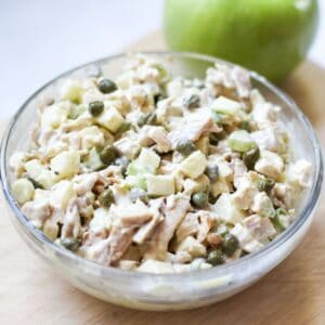 Creamy chicken salad with cubed and diced ingredients in a large bowl. There is a whole green apple behind the bowl.