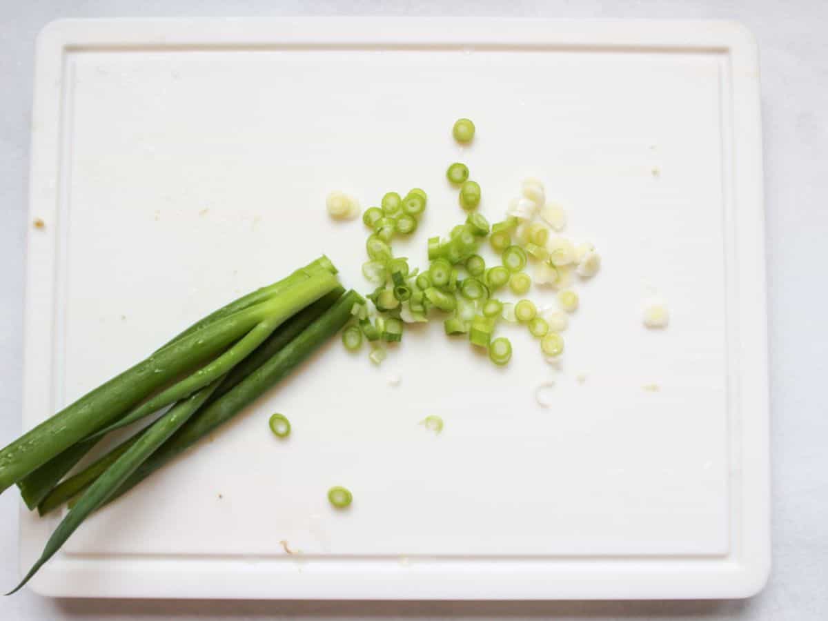 Green scallion on a white cutting board. The half of the scallion is diced finely.