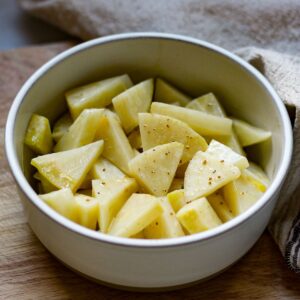 Sliced celery root cut into triangle slices in a white bowl. The bowl is on a wooden surface.