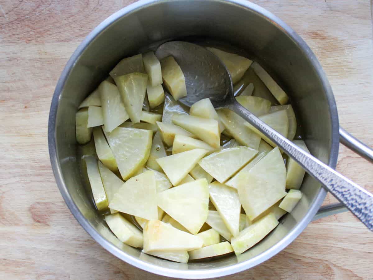 Thinly sliced white root vegetable in a stainless steel pot with a spoon in it.
