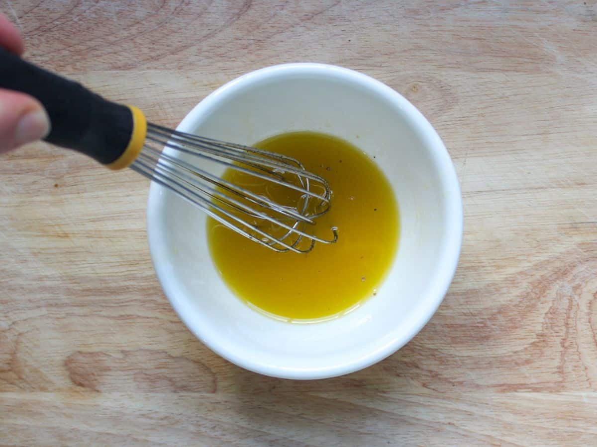 Yellow olive oil based dressing in a small bowl with a whisk in it.