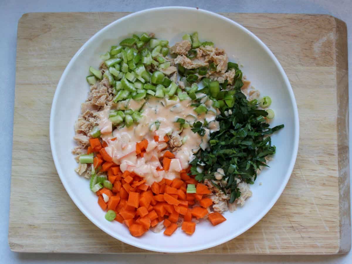 Chopped and diced tuna salad ingredients drizzled with buffalo dressing in a white shallow dish .