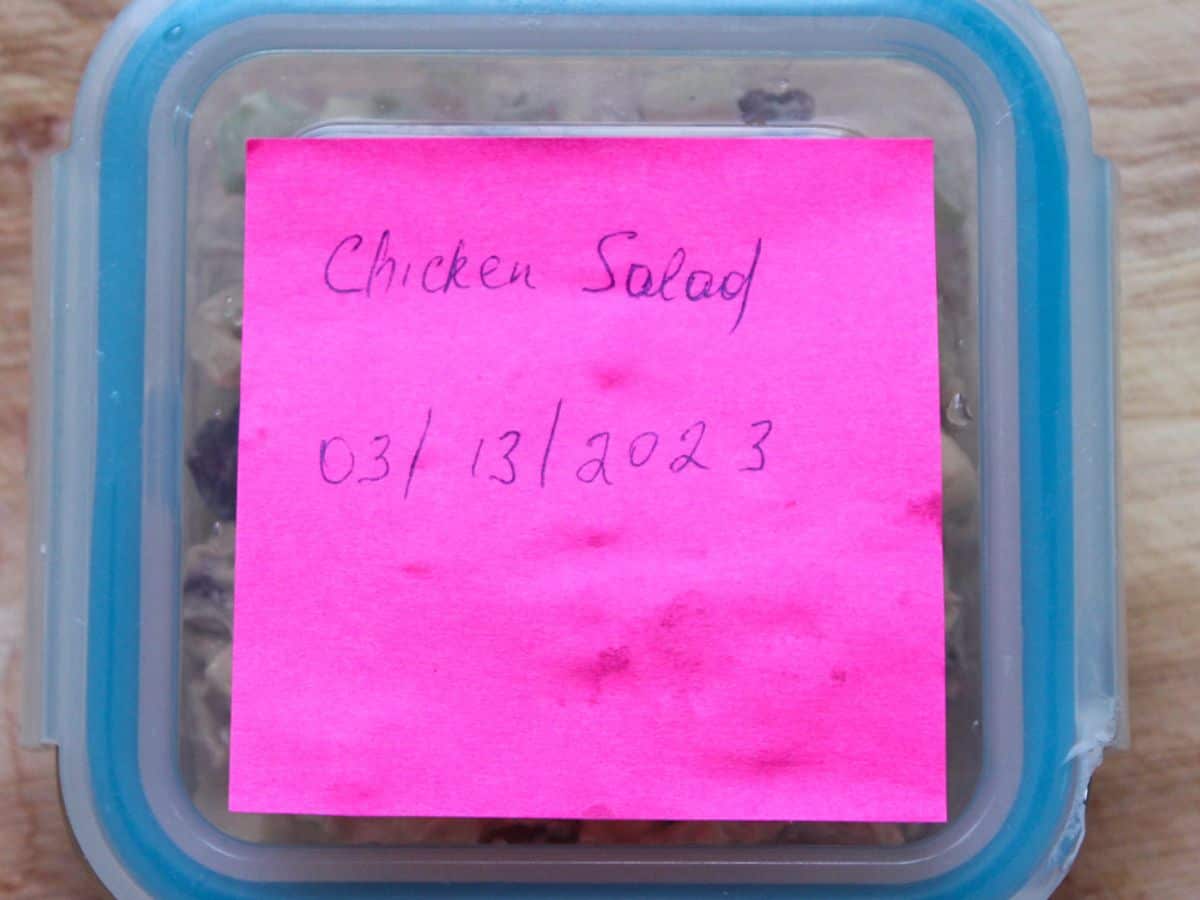 A square container with a lid on it labeled as "chicken salad 03/13/2023
