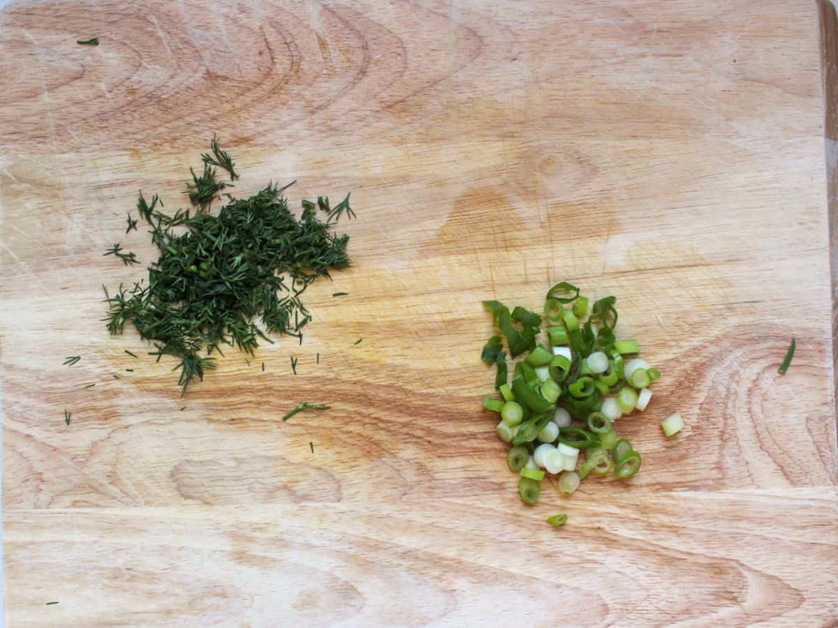 Two heaps of chopped dill and green onions on a cutting board.