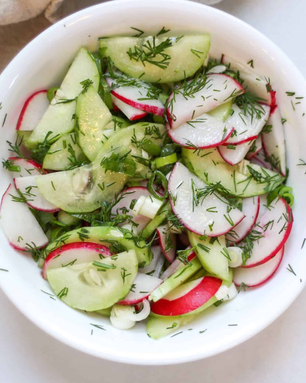 Cucumber and radish salad with fresh dill in a white bowl.