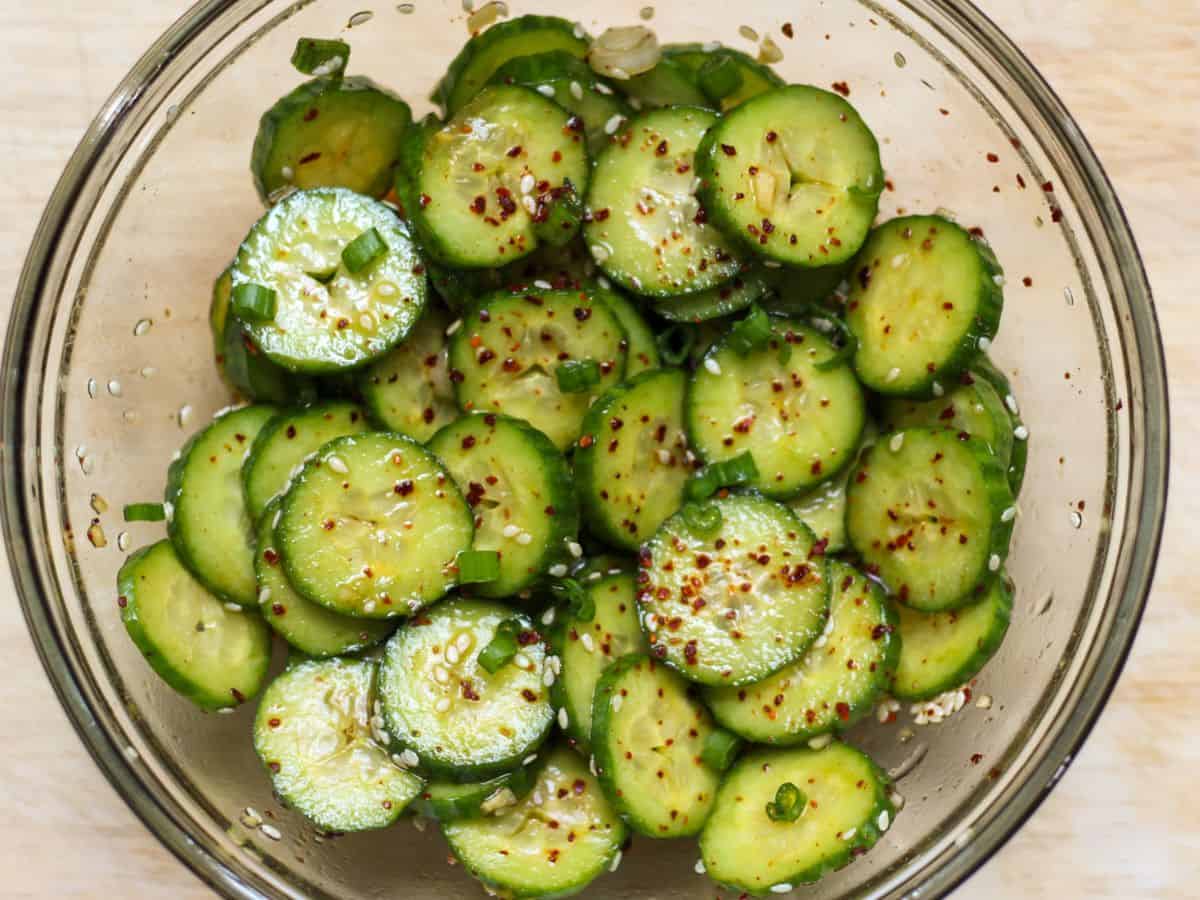 Thinly sliced cucumbers tossed in a spicy dressing in a glass bowl.