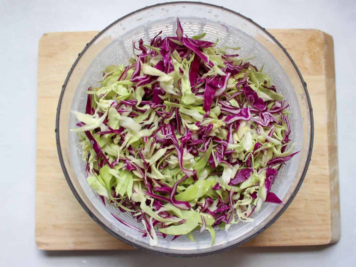 Shredded green and purple cabbage in a salad spinner.