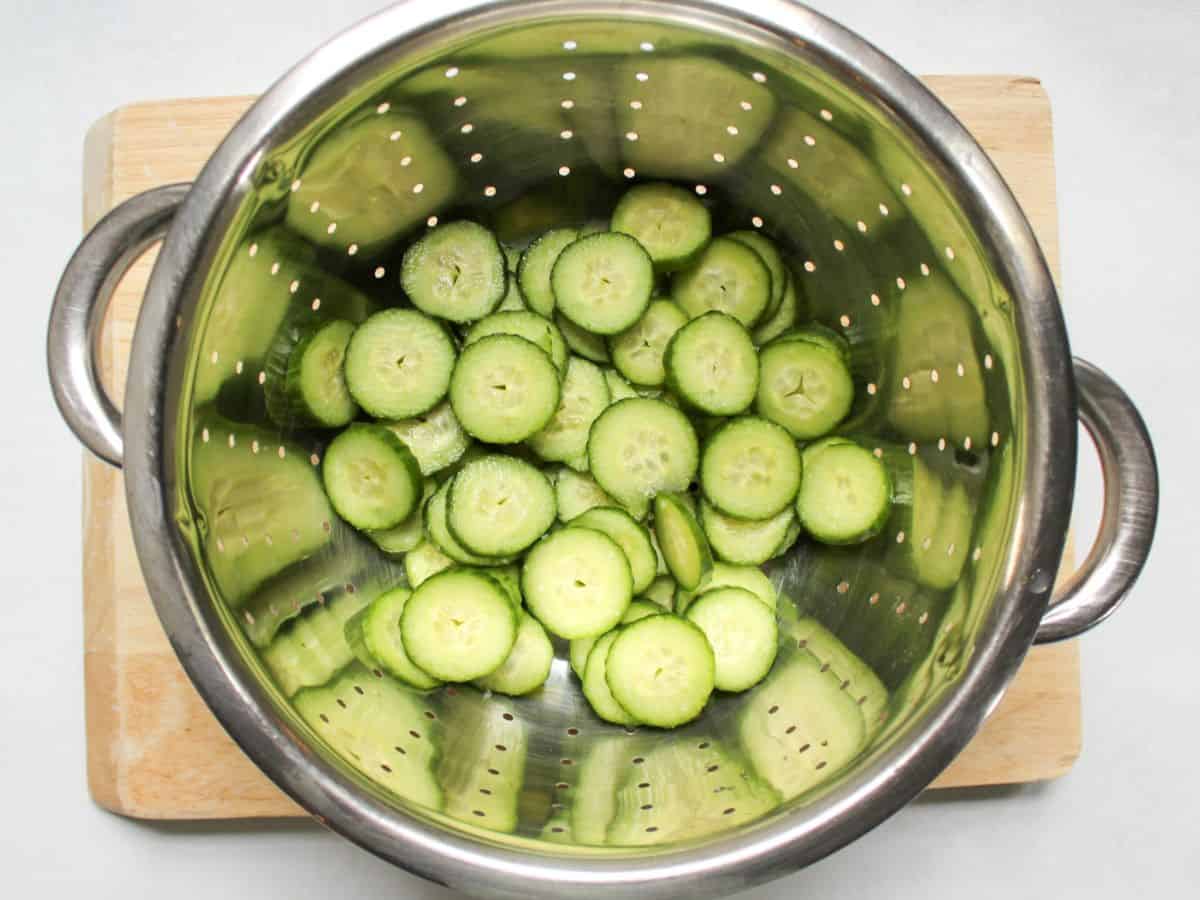 Sliced cucumbers in a stainless steel colander.
