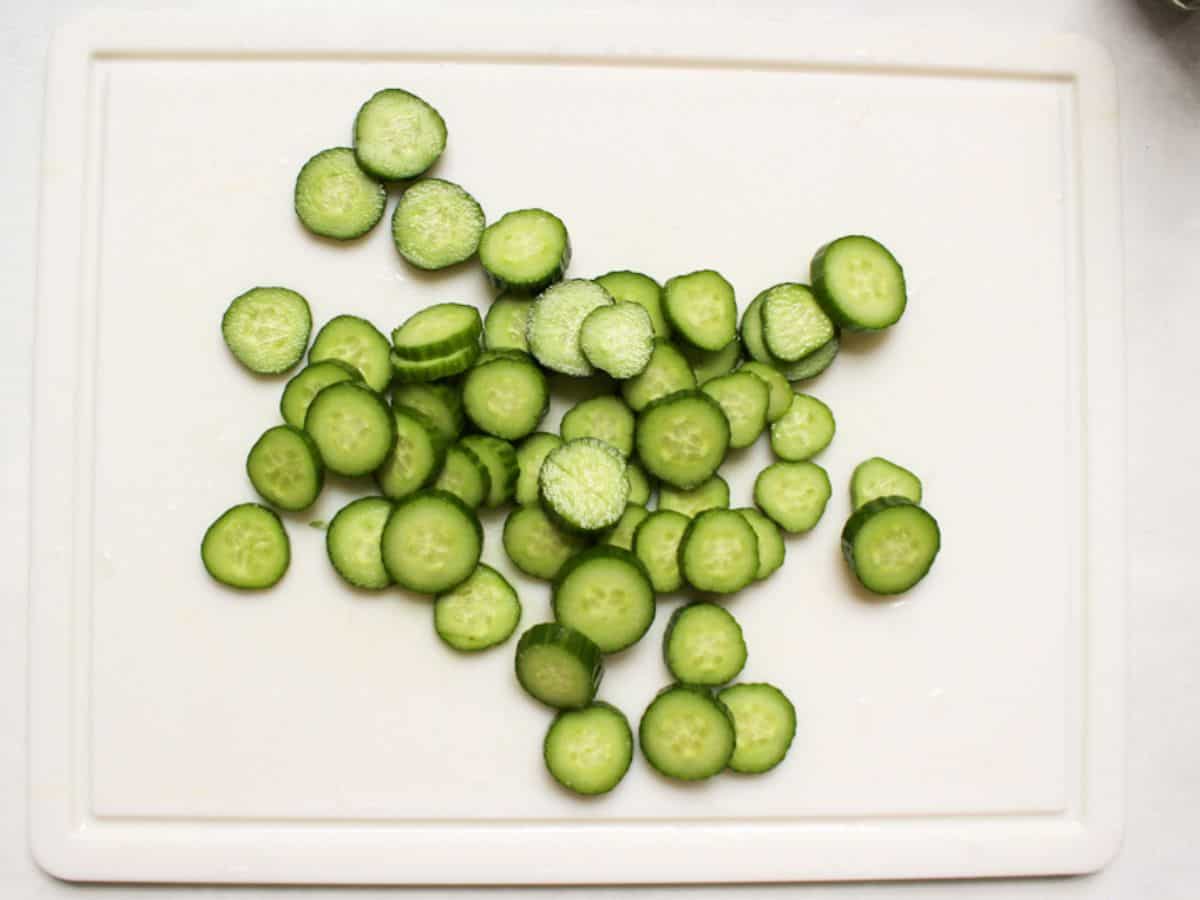 Thinly sliced fresh cucumbers on a white board.