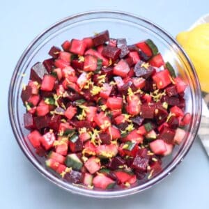 Beet and cucumber salad in a large glass bowl garnished with lemon zest on top.