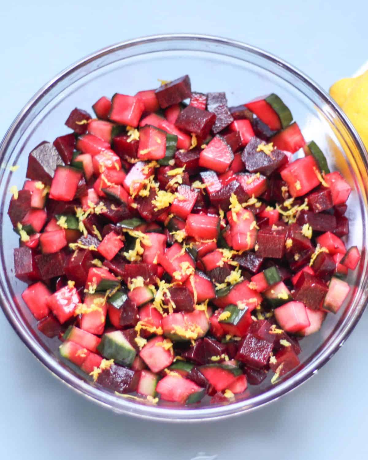 Beet and cucumber salad in a large glass bowl garnished with lemon zest on top.