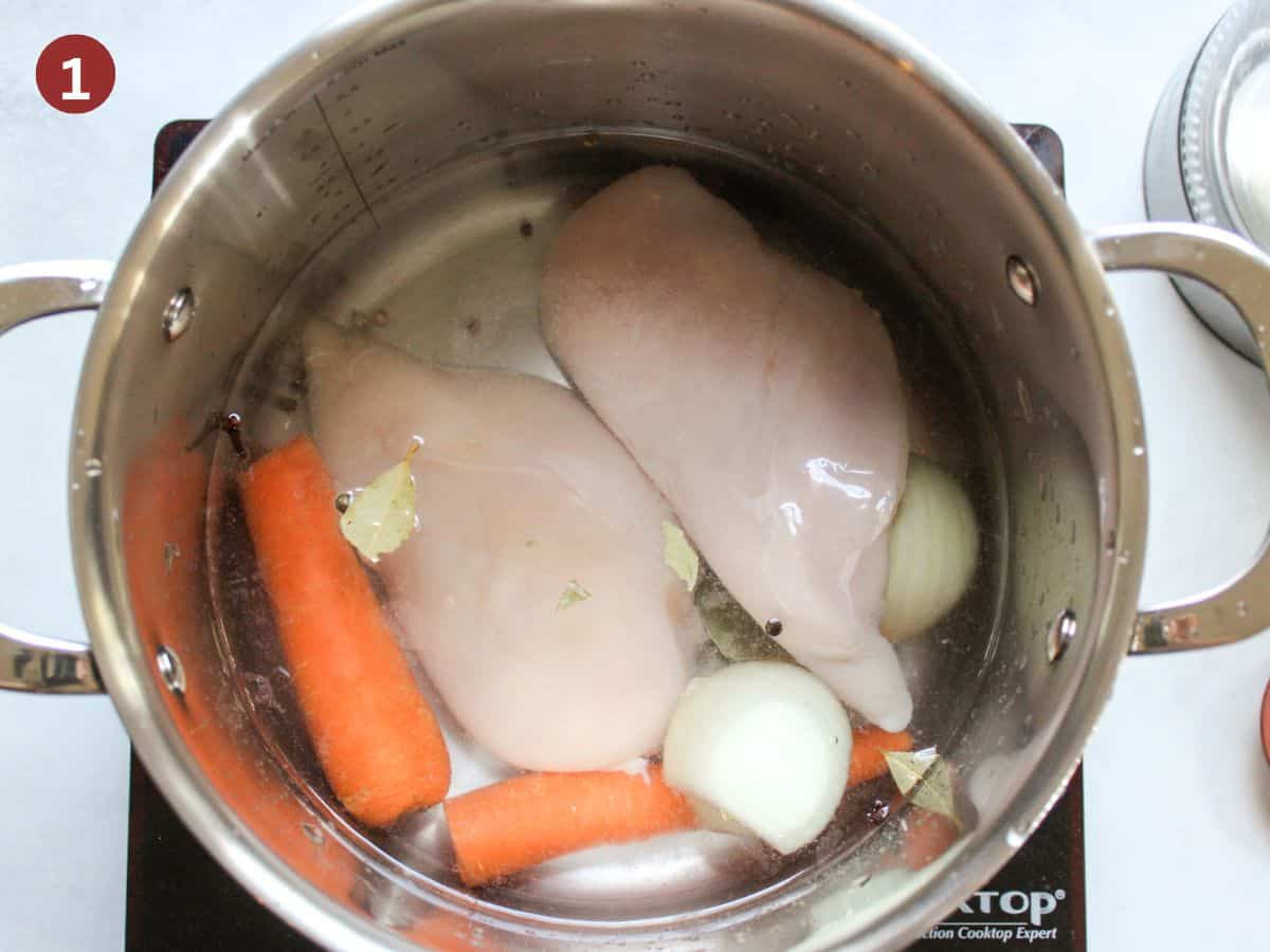 Raw chicken breasts added to the pot, along with onion, carrot, bay leaf and water.