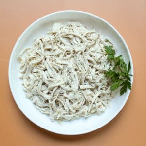 Tender shredded poached chicken breast on a white plate – perfect for salads, sandwiches, or meal prep.