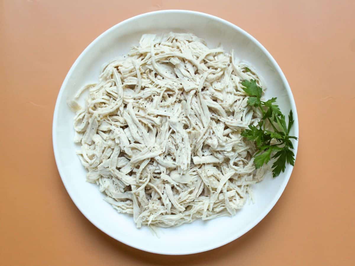 Shredded poached chicken breast arranged on a white plate, ready to use in chicken salad.